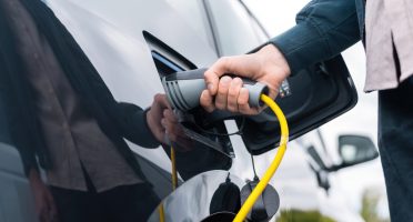 Man plugging in charger into an electric car at charge station