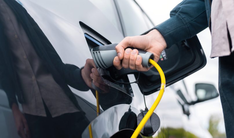 Man plugging in charger into an electric car at charge station
