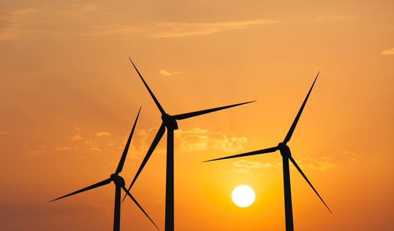 Green renewable energy concept - wind generator turbines in sky on sunset